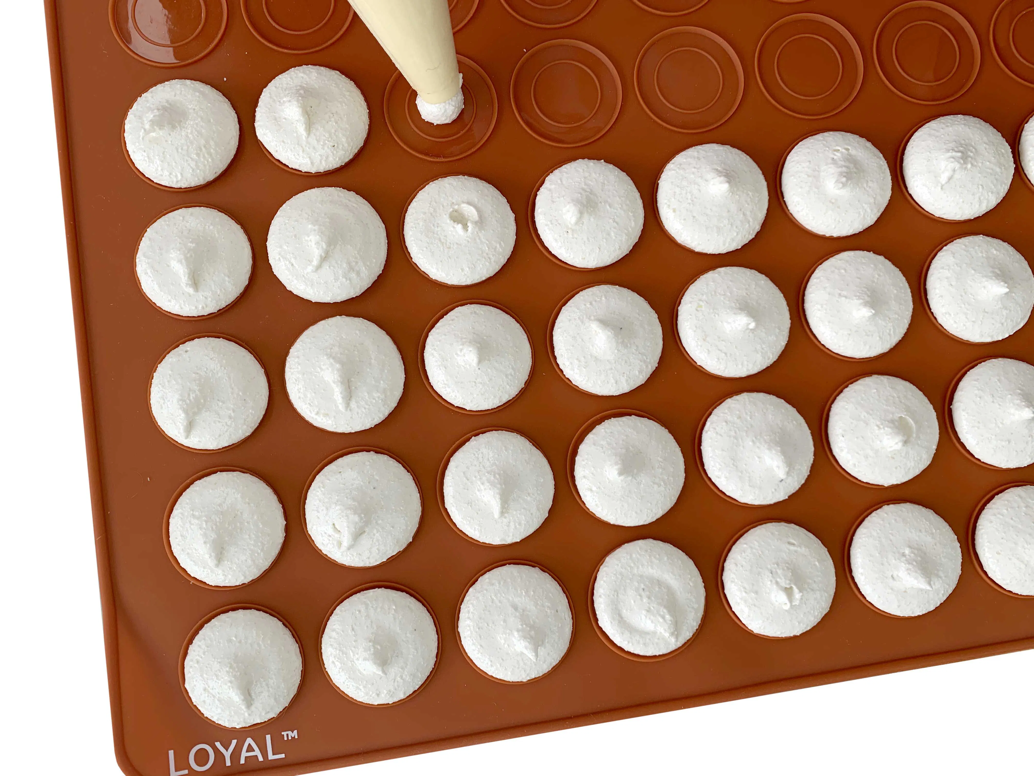 Macarons being piped onto the macaron templates of silicone mat